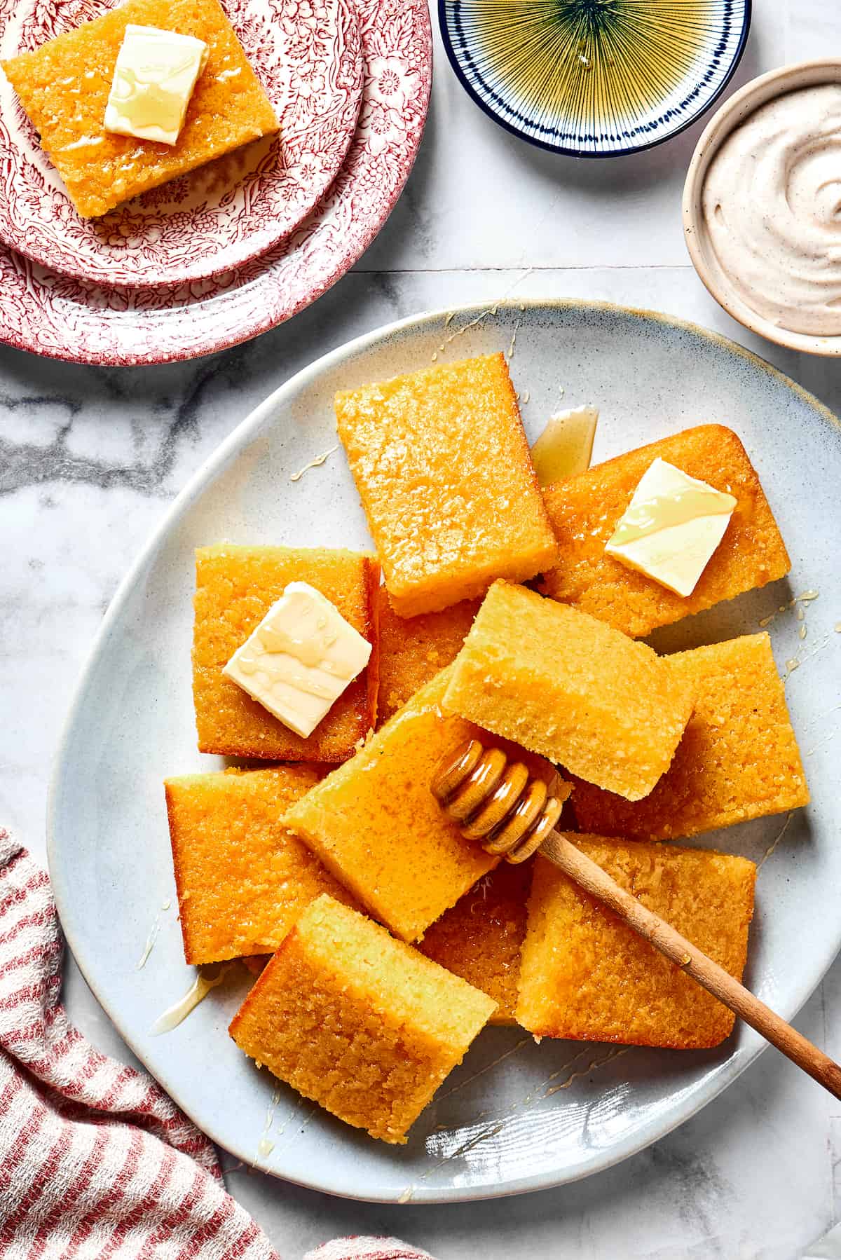 Squares of cornbread on a plate with pats of butter and a small honey dipper.