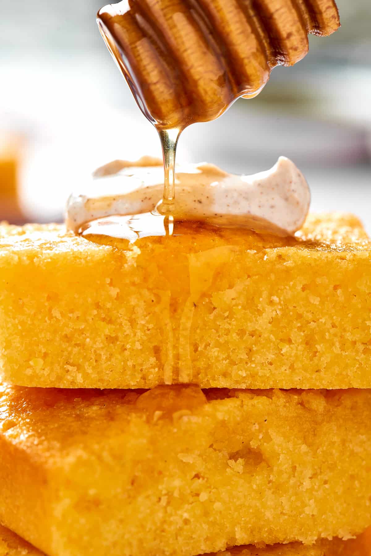 A honey dipper drizzling honey over squares of cornbread with cinnamon cream.