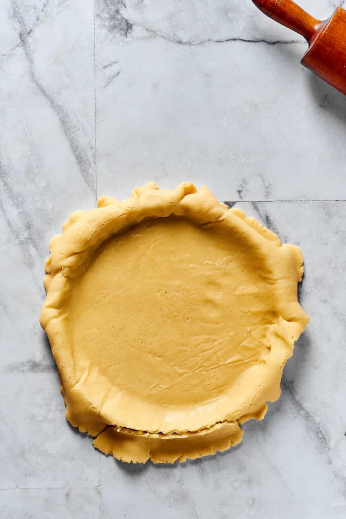 A rolled-out pie crust in a dish, with the edges overhanging the dish.