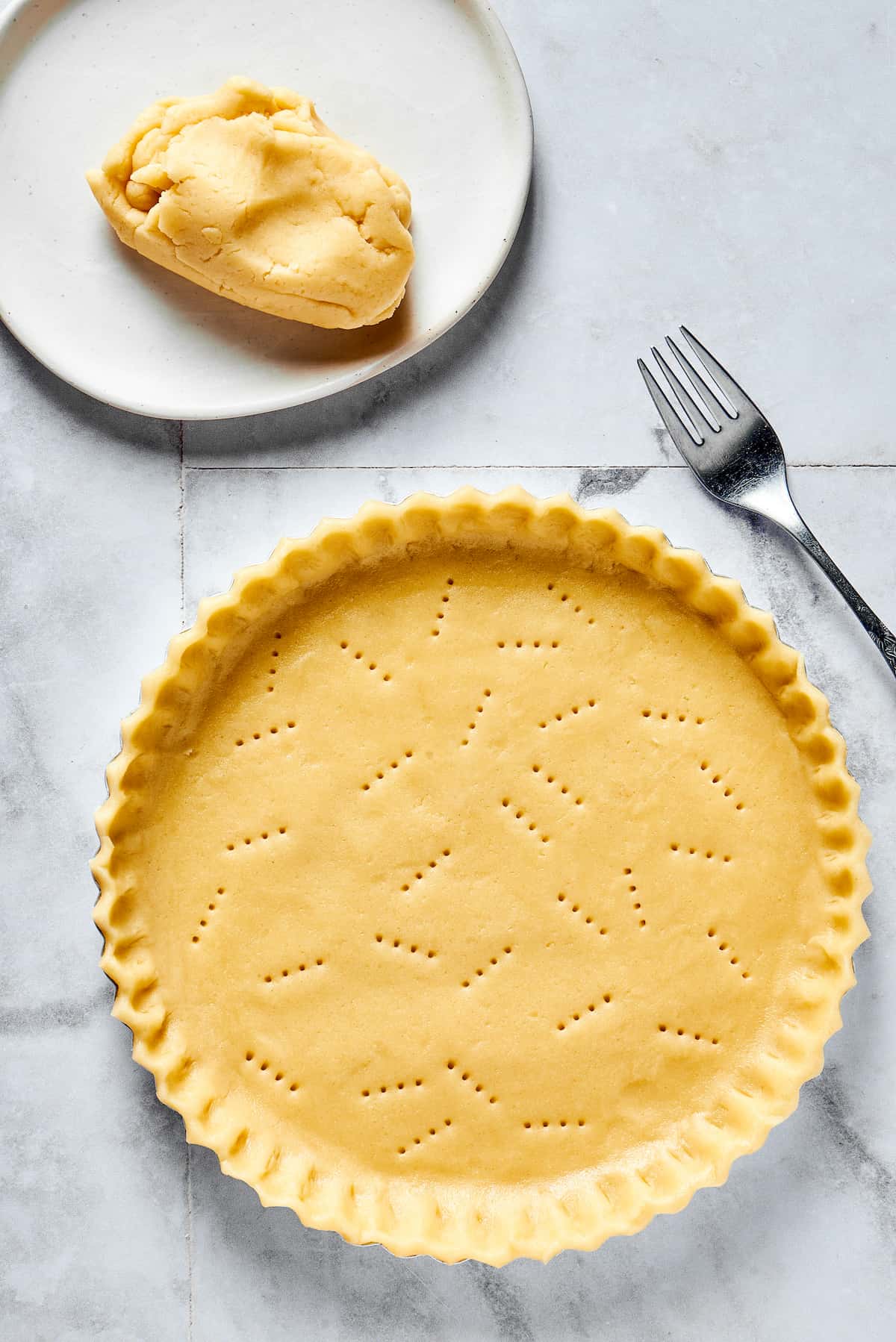 Pie dough pressed into a pie dish with the edges trimmed. The crust has been pricked with a fork.