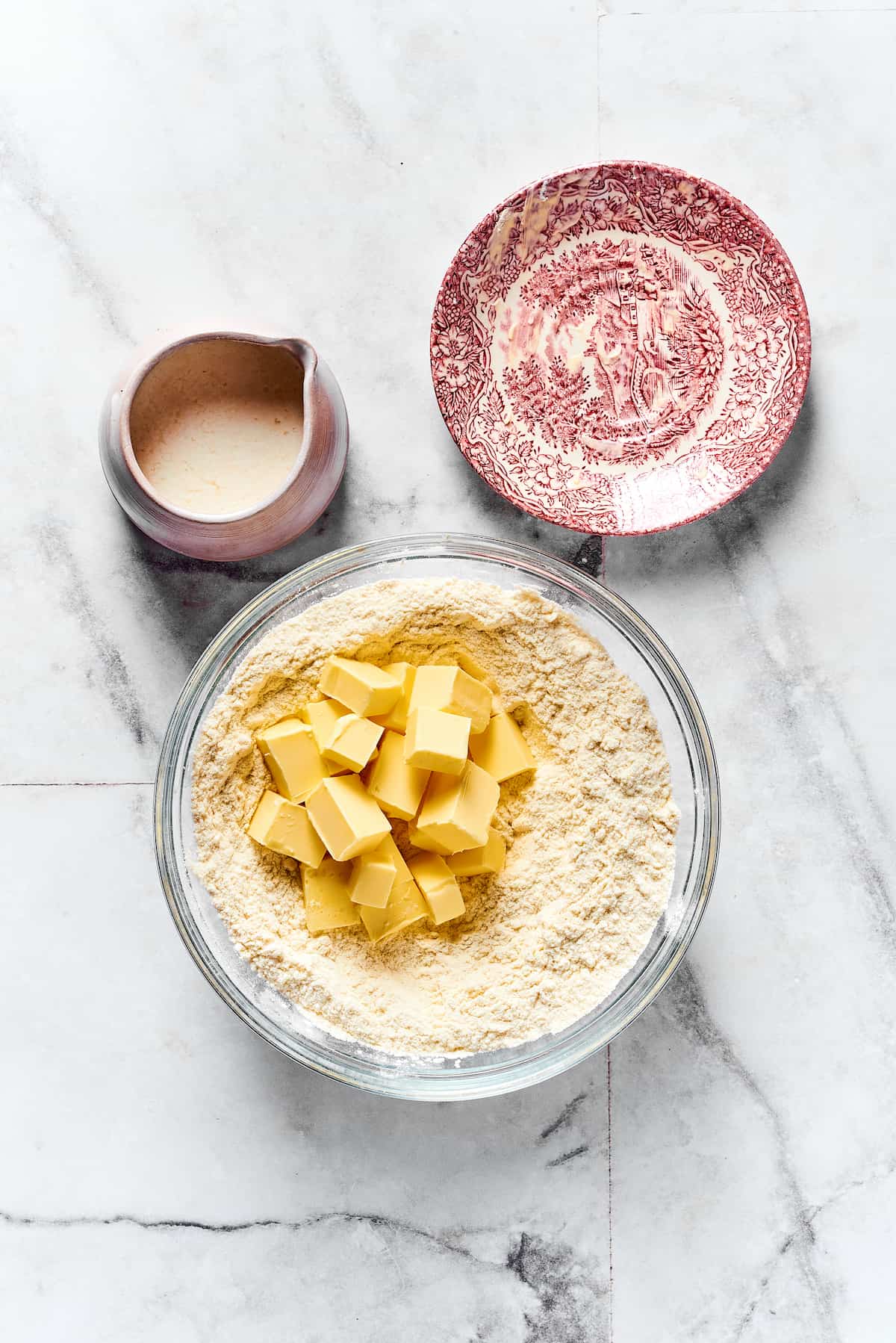 Butter cubes being added to dry ingredients in a mixing bowl.