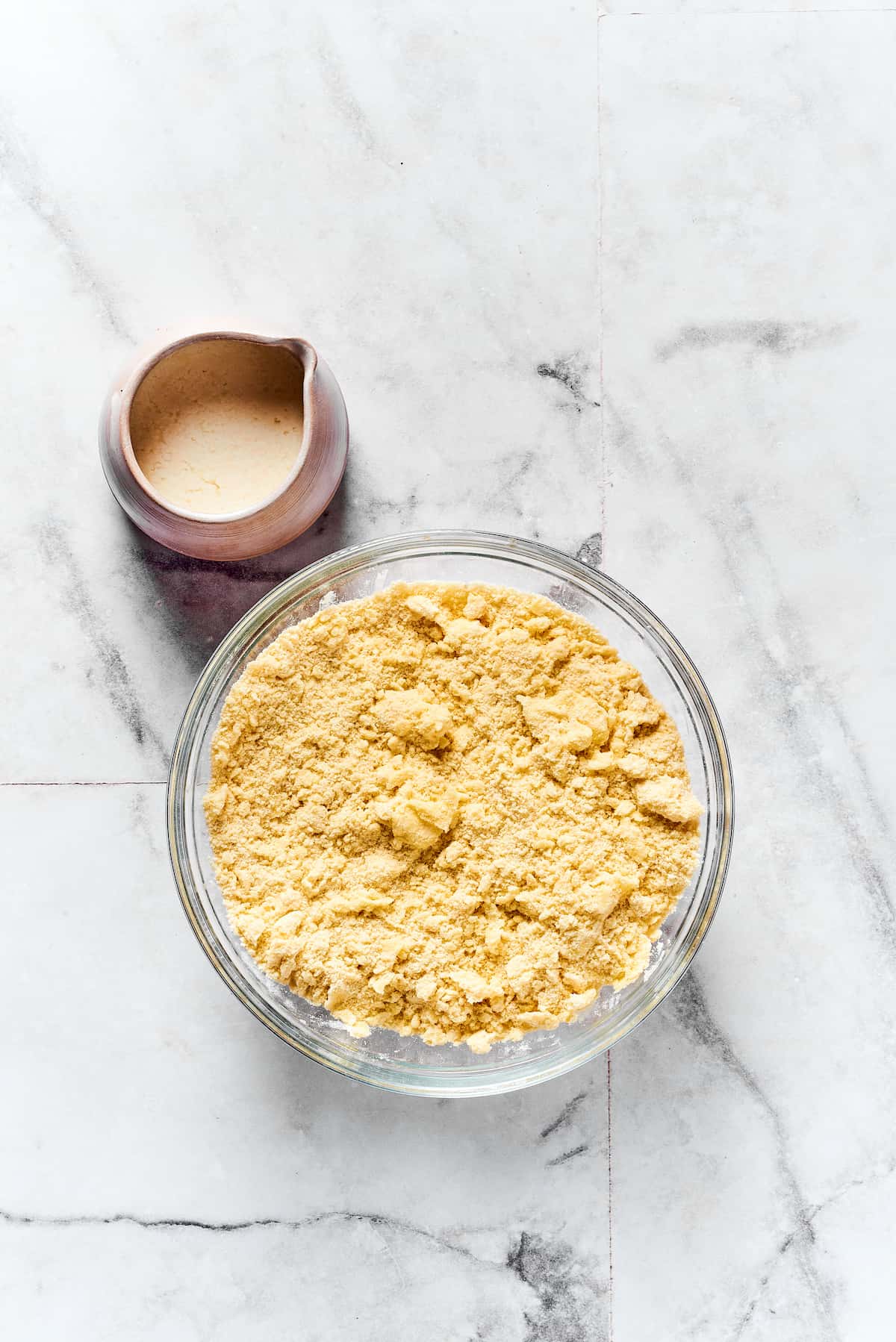 A mixing bowl of dry biscuit ingredients next to a small pitcher of buttermilk.