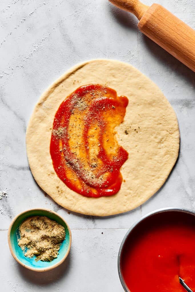 Pizza sauce and seasonings spread on a circle of dough.