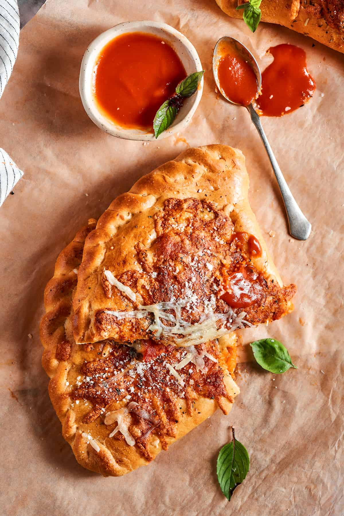 A calzone cut in half on a parchment-lined surface next to a bowl of dipping sauce.