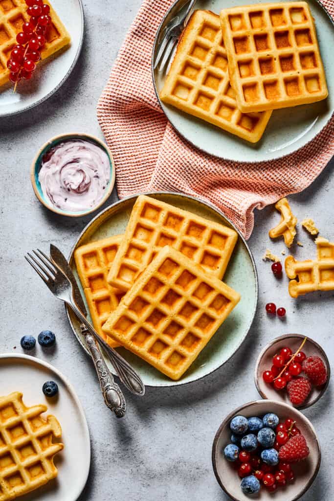 Breakfast made with a homemade waffle recipe. The waffles are arranged on a table with cloth napkins, berries, and yogurt.