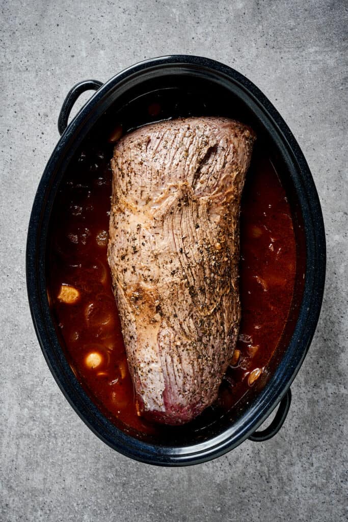 Rump roast in a Dutch oven with broth and other ingredients.