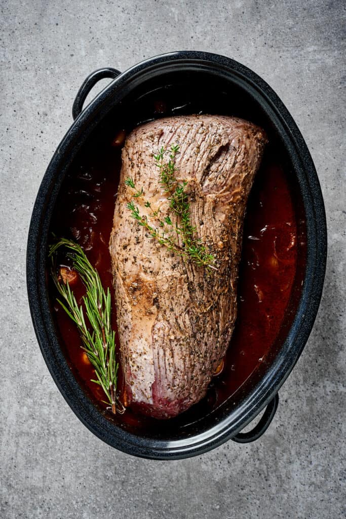 Rump roast with fresh herbs and cooking liquid in a Dutch oven.
