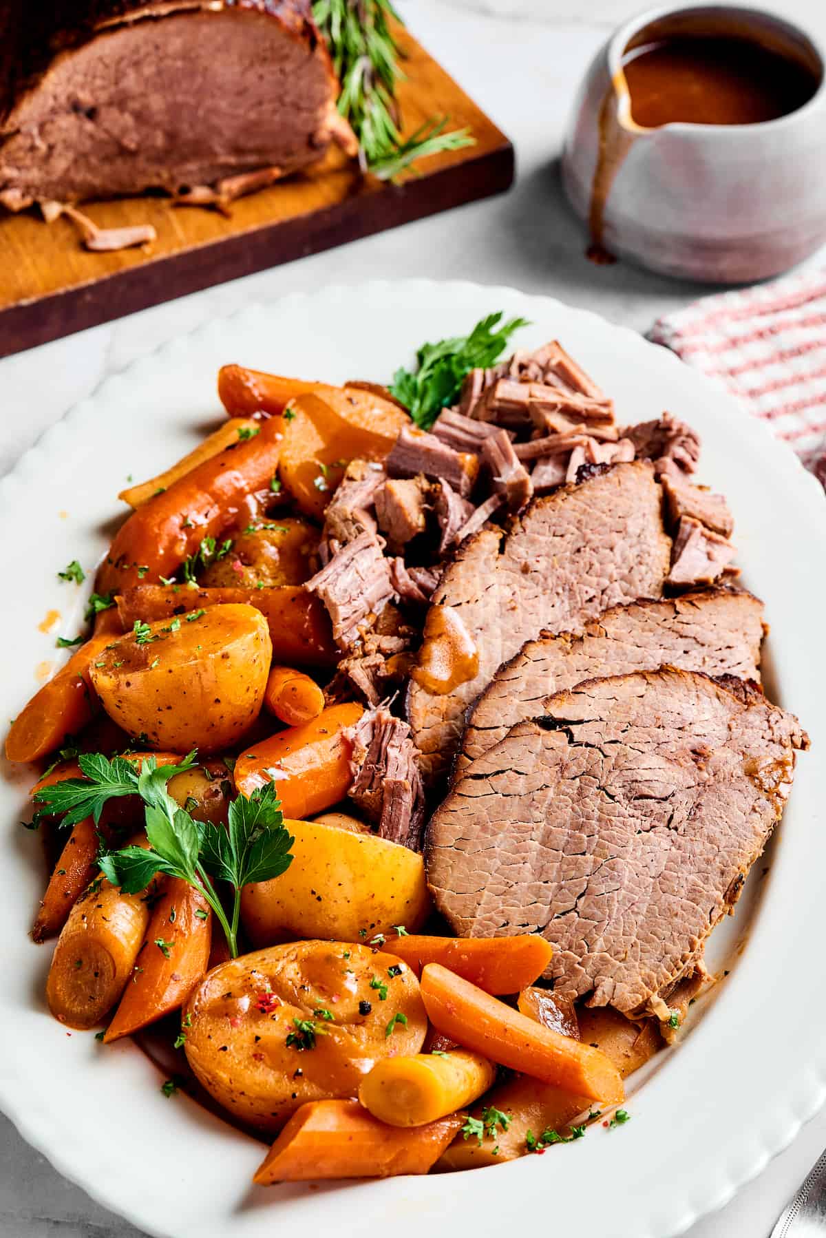 A platter of pot roast with vegetables next to a carving board with roast beef, and a pitcher of gravy.