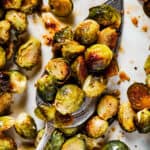 A tray of roasted brussel sprouts with a silver serving spoon.