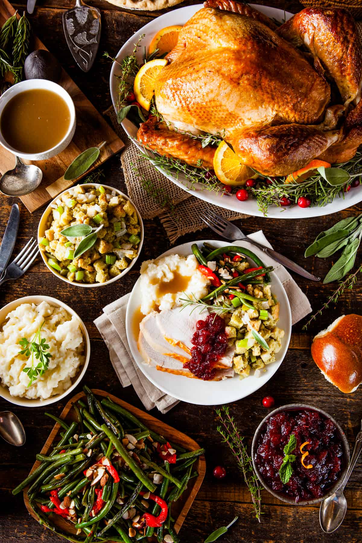 overhead shot of a whole turkey at the top of the photo, then a bowl of mashed potatoes, stuffing, green beans, and cranberry sauce.