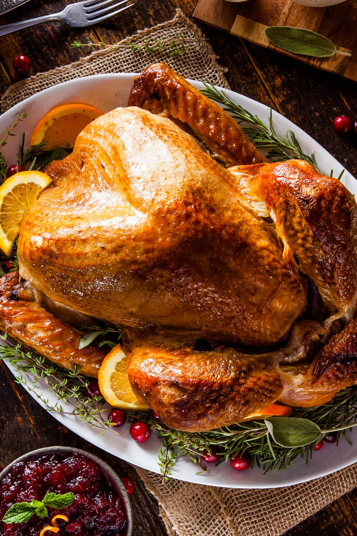 A roasted Thanksgiving turkey garnished with citrus slices and green herbs.