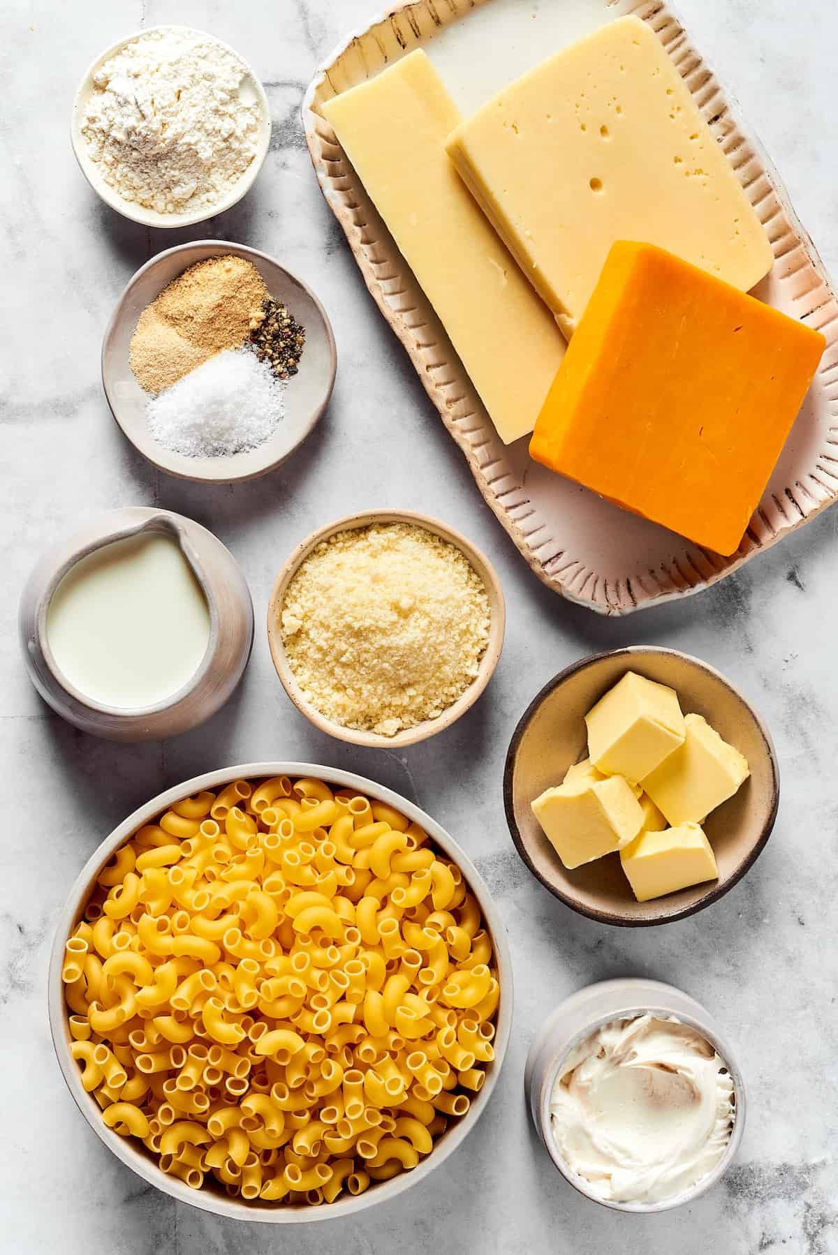 From top left: Flour, gouda cheese, mozzarella cheese, cheddar cheese, seasonings, milk, parmesan, butter, macaroni, heavy cream.