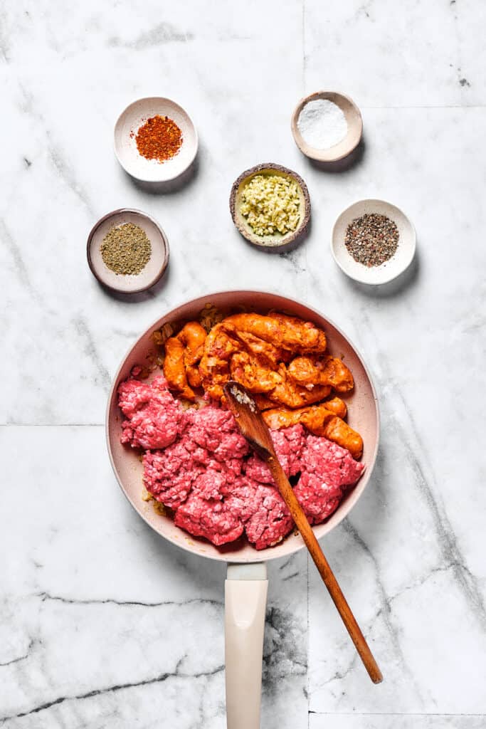 Italian sausage and ground beef cooking in a skillet.