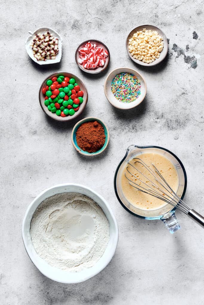 Cake mix cookie ingredients. The dry and wet ingredients are blended together in separate bowls, while the decorations and cocoa powder are still in small dishes on the table.