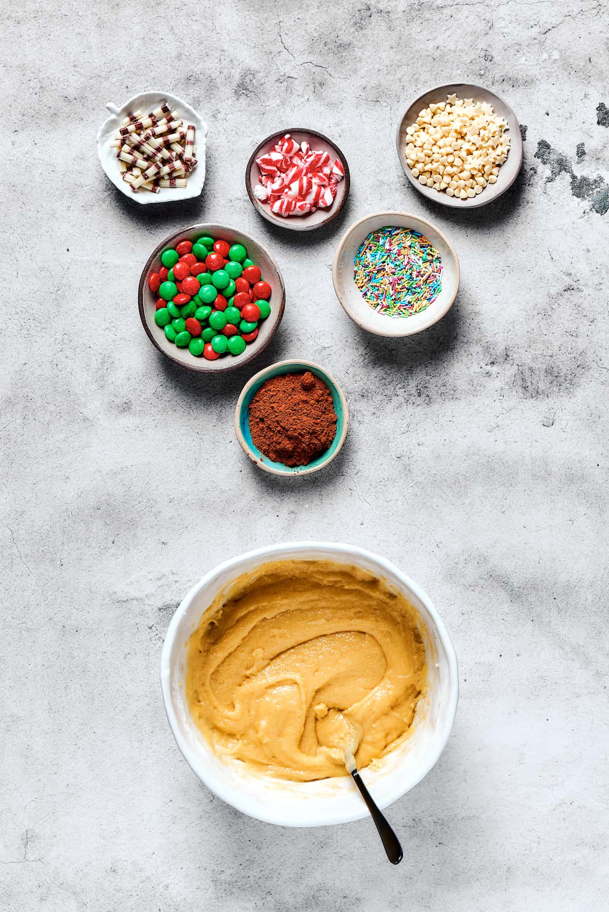 A bowl of cookie dough next to small dishes of decorations.