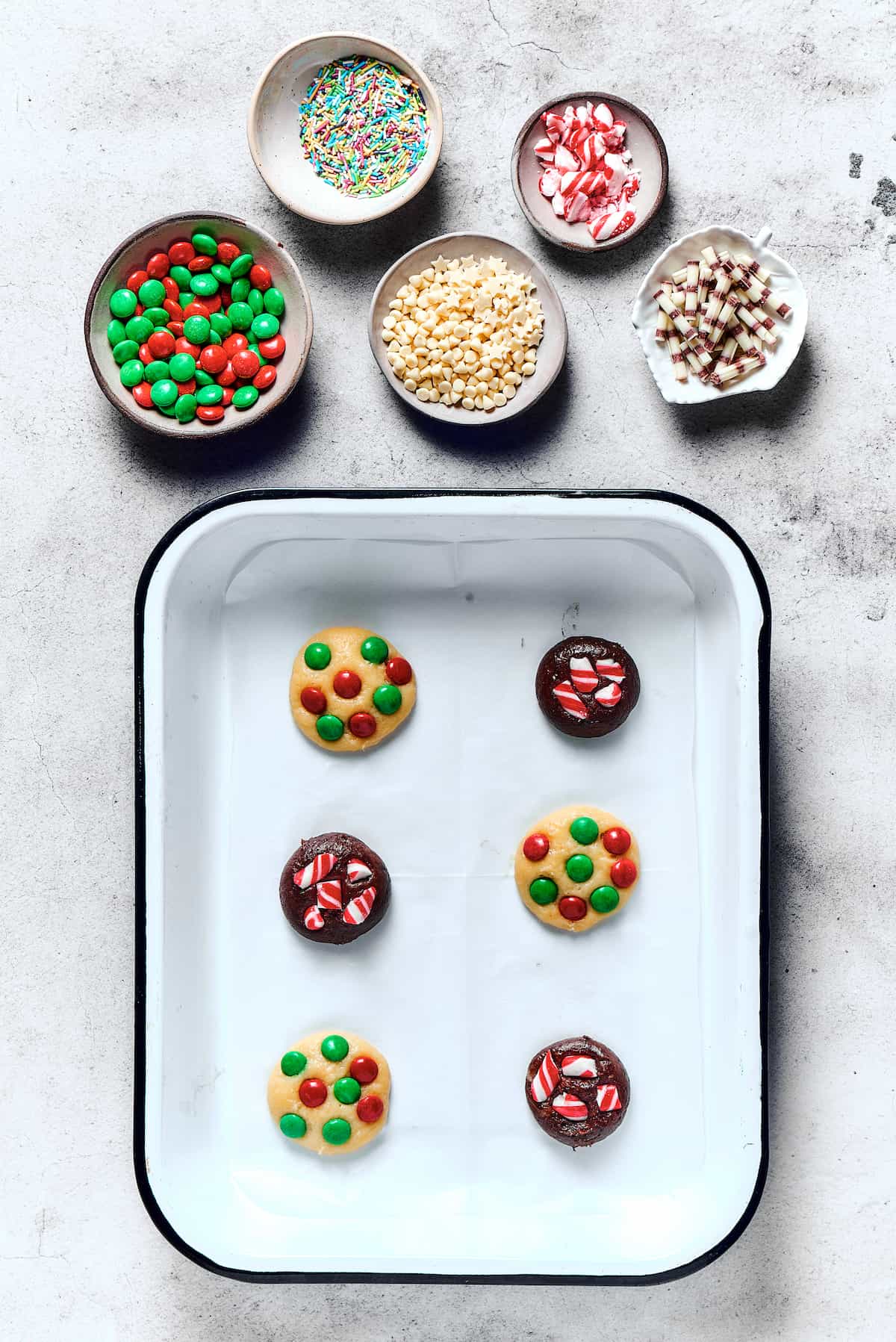 Unbaked chocolate and vanilla cookies on a baking sheet, with M&M's pressed into the dough.