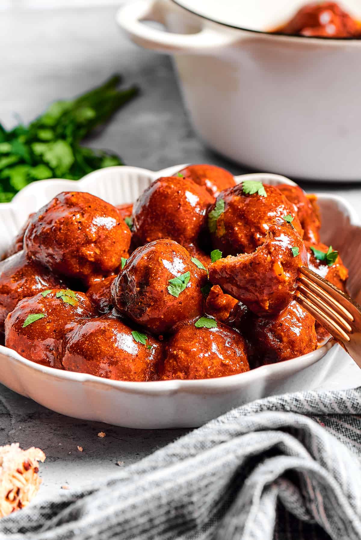 A large white dish of grape jelly meatballs, with a smaller plate of them nearby.