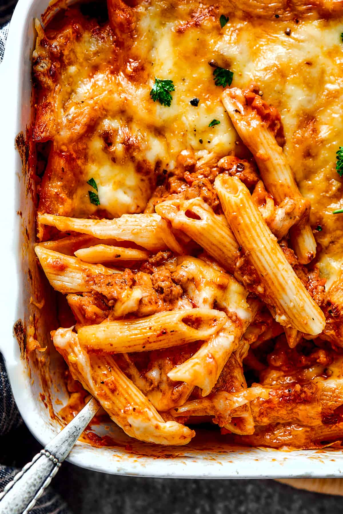 Scooping out a spoonful of baked mostaccioli from a large baking dish.