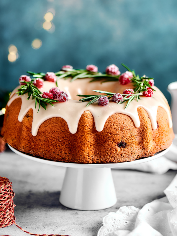 cranberry cake on a white cake stand, with lights in the background of the shot.