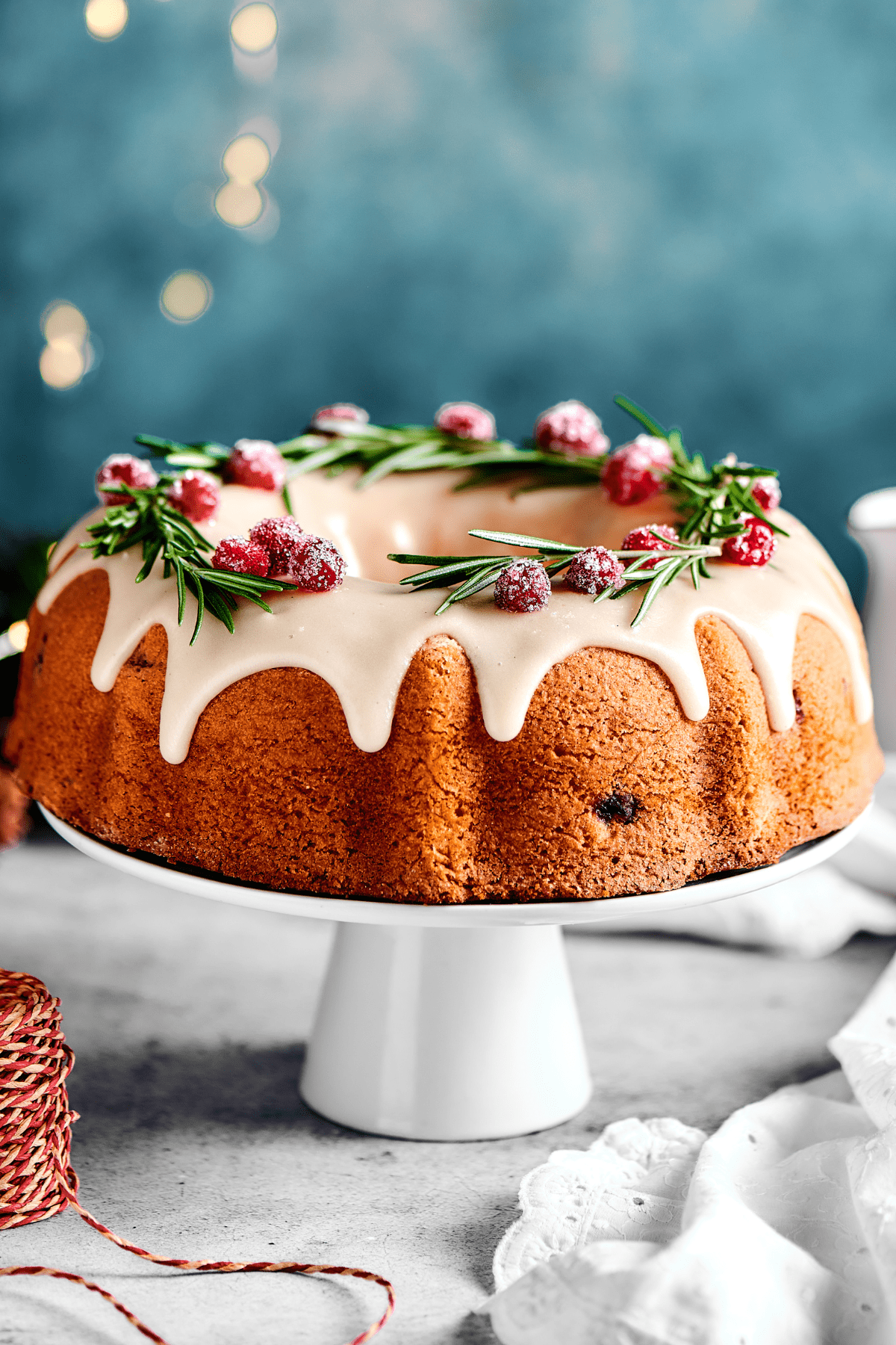 A cranberry pound cake on a white cake stand, with lights in the background of the shot.