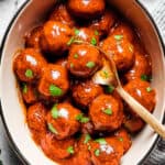 A white serving deep dish of meatballs with a spoon.