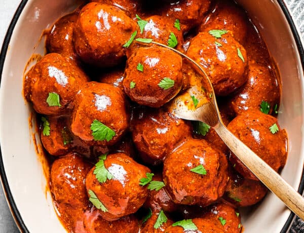 A white serving deep dish of meatballs with a spoon.