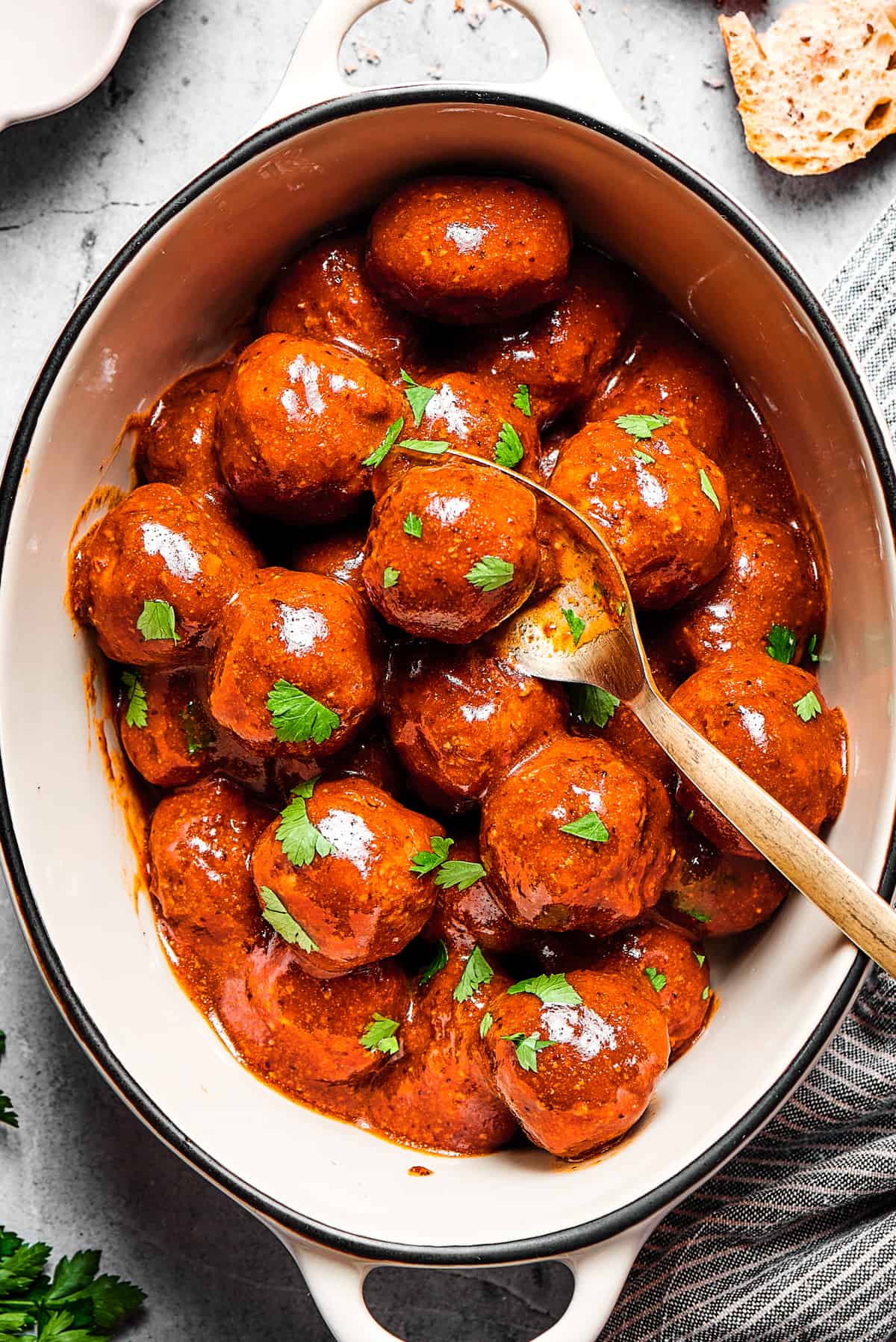 A white serving deep dish of meatballs with a spoon.