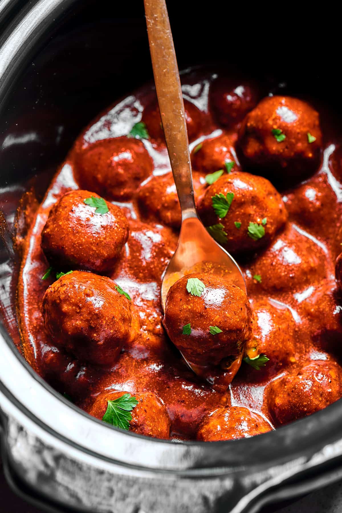 A slow cooker viewed from the top, filled with grape jelly meatballs.