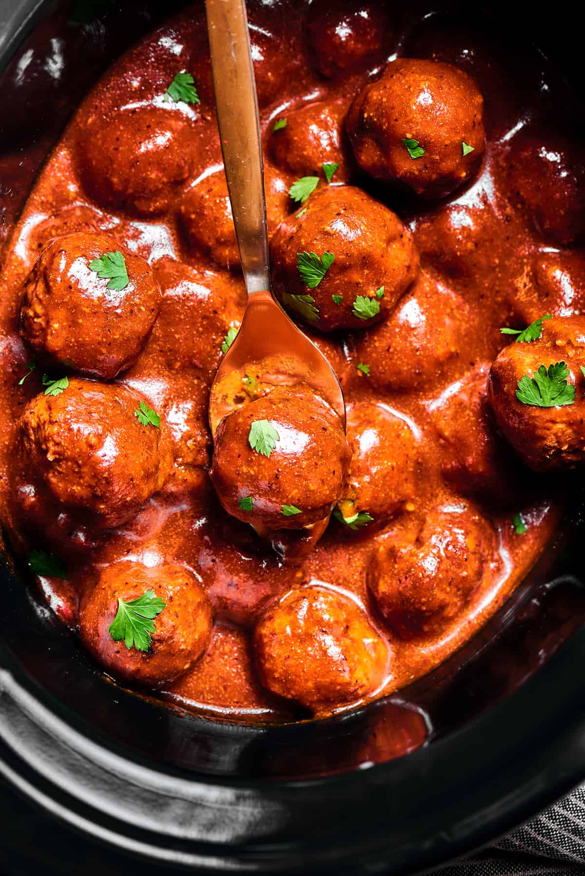 slow cooker Meatballs in sauce, sprinkled with parsley.