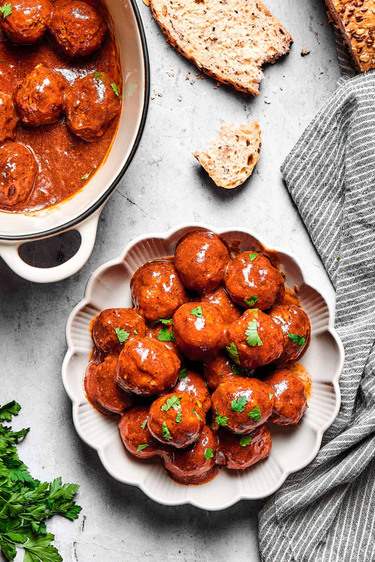 A plate with fluted edges, heaped with grape jelly meatballs, next to a larger serving dish.