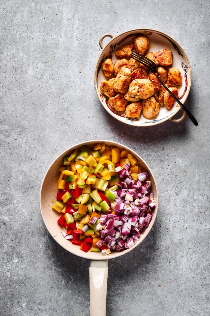 Chopped vegetables in a skillet next to a bowl of cooked chicken.