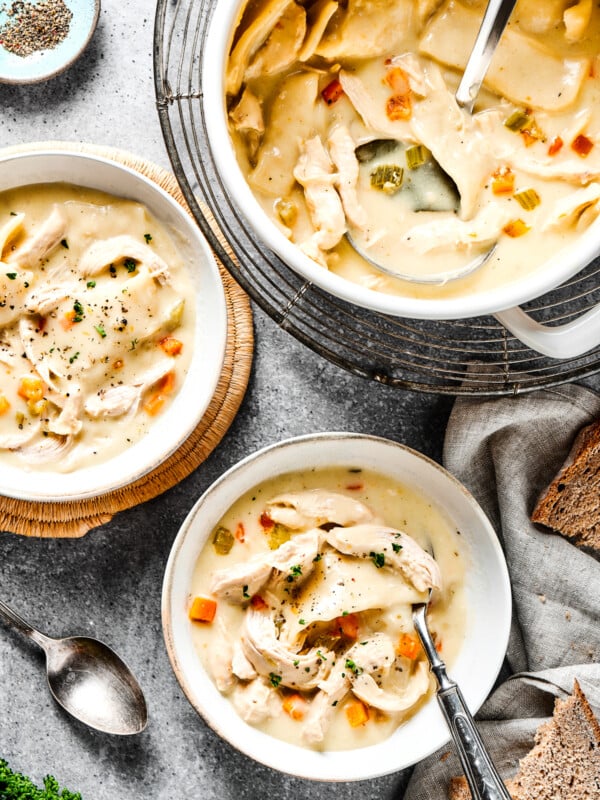 Creamy chicken and dumplings in a pot, along with two bowls of the dish.