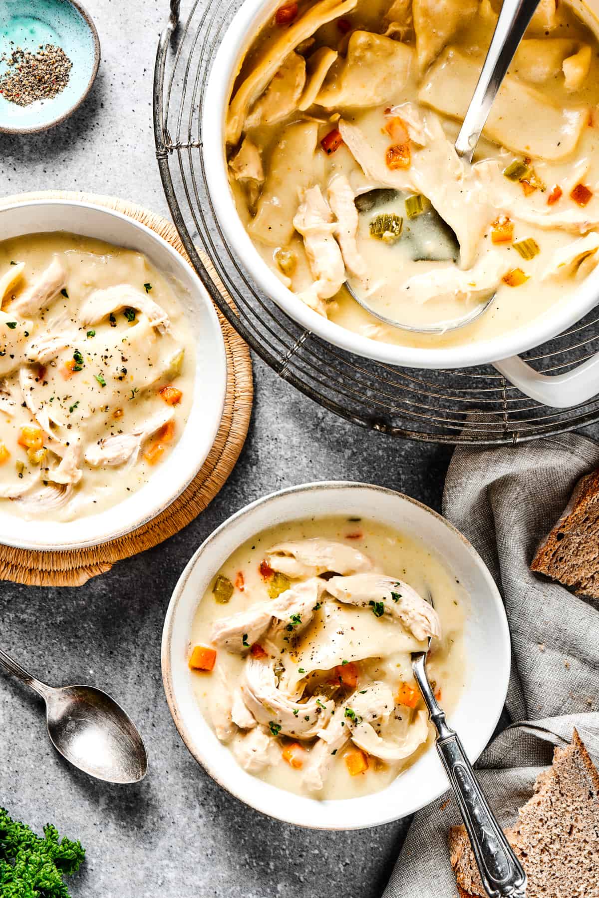 Creamy chicken and dumplings in a pot, along with two bowls of the dish.