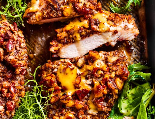 Sliced pecan chicken on a serving dish, with greens placed around the chicken.