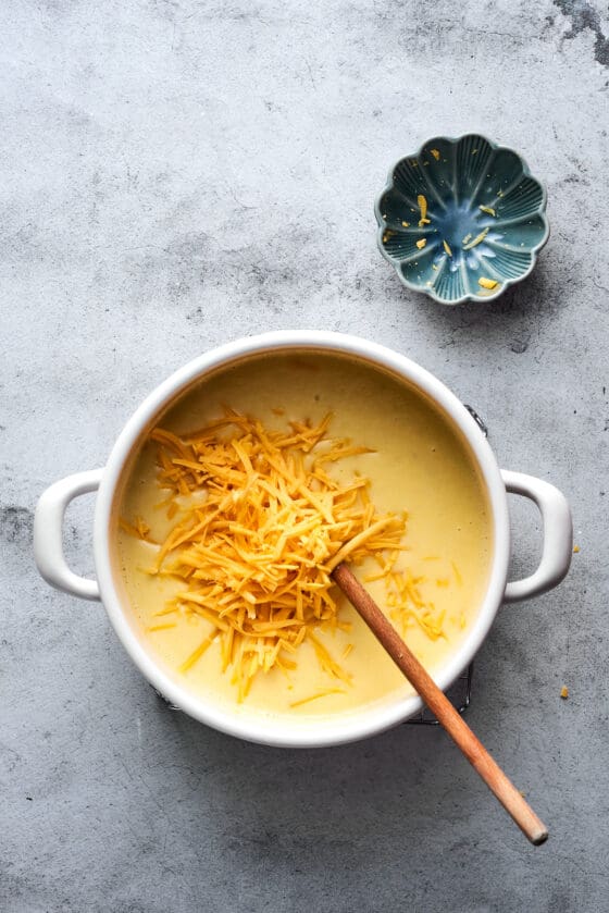 Shredded cheddar added to a pot of soup.
