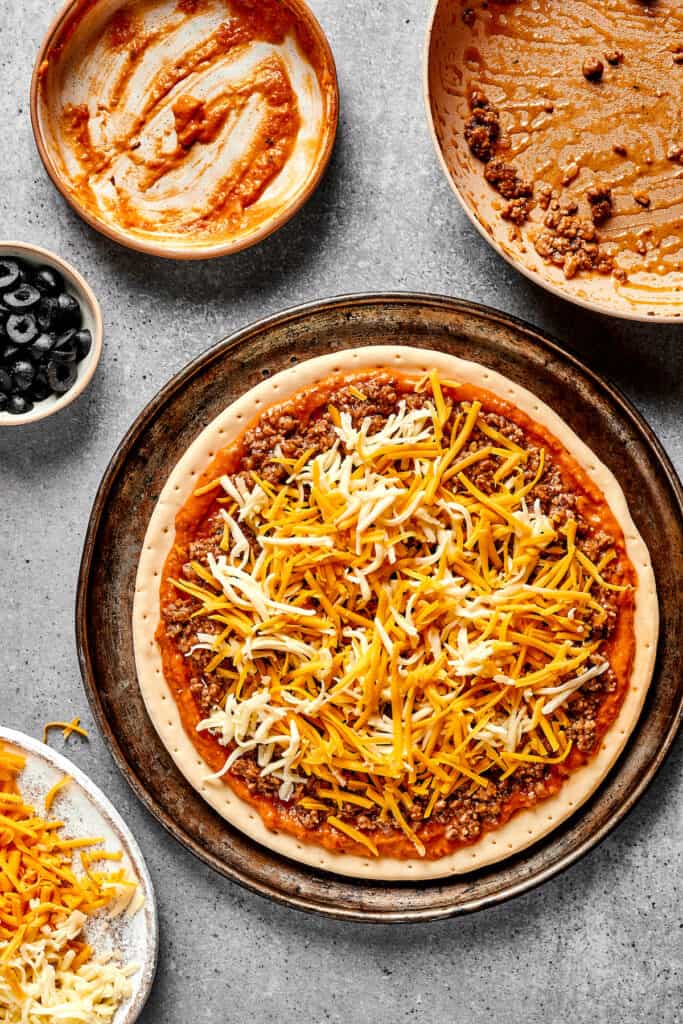A pizza crust topped with refried bean sauce, beef, and cheese.