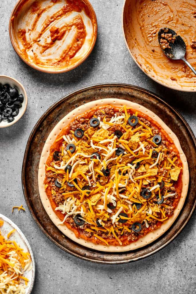 Black olives sprinkled on an unbaked Mexican pizza.