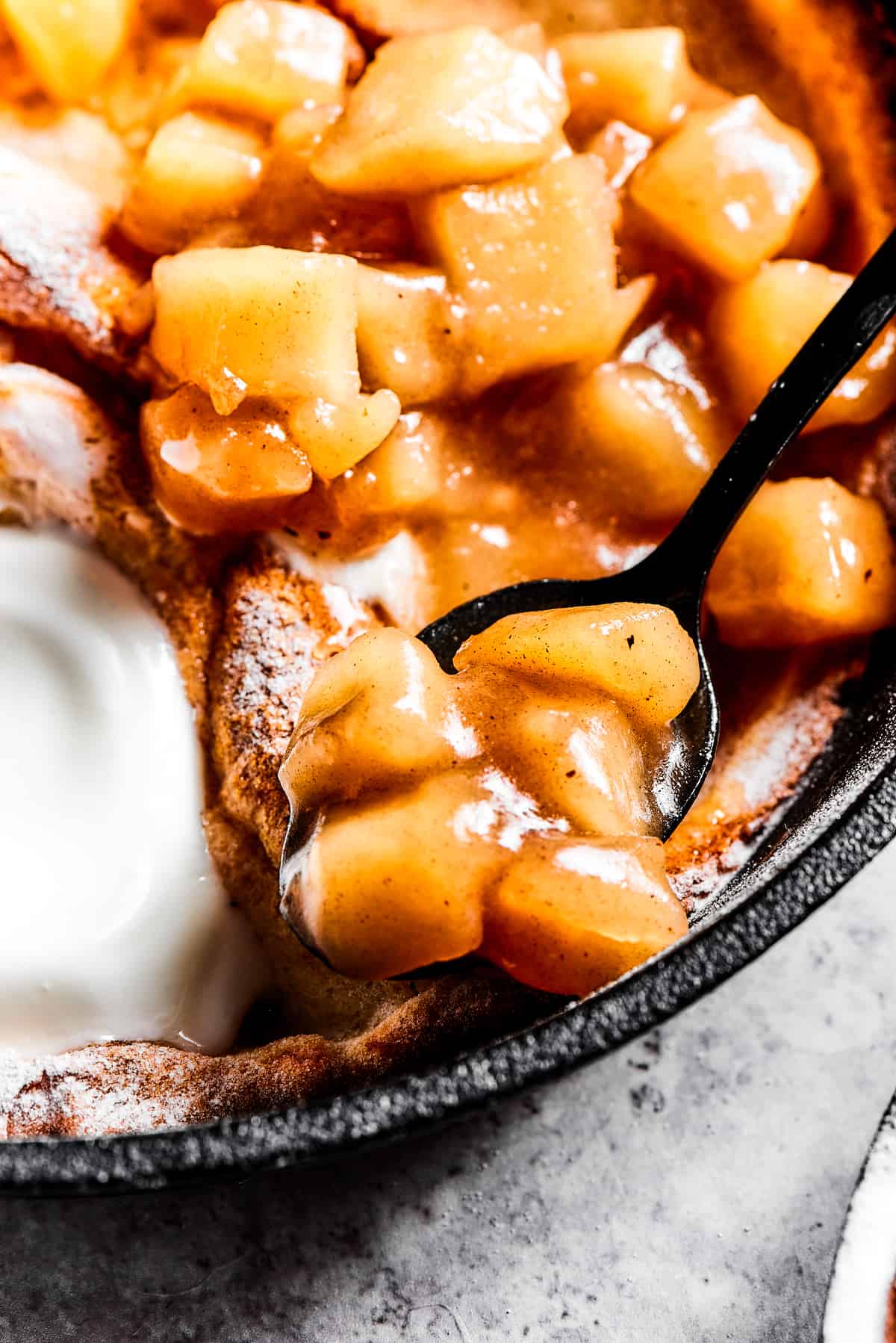 spooning apple pie filling on top of a dutch baby pancake.