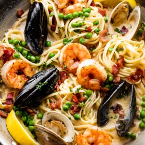 a skillet with pasta, shrimp, and mussels in cream sauce.