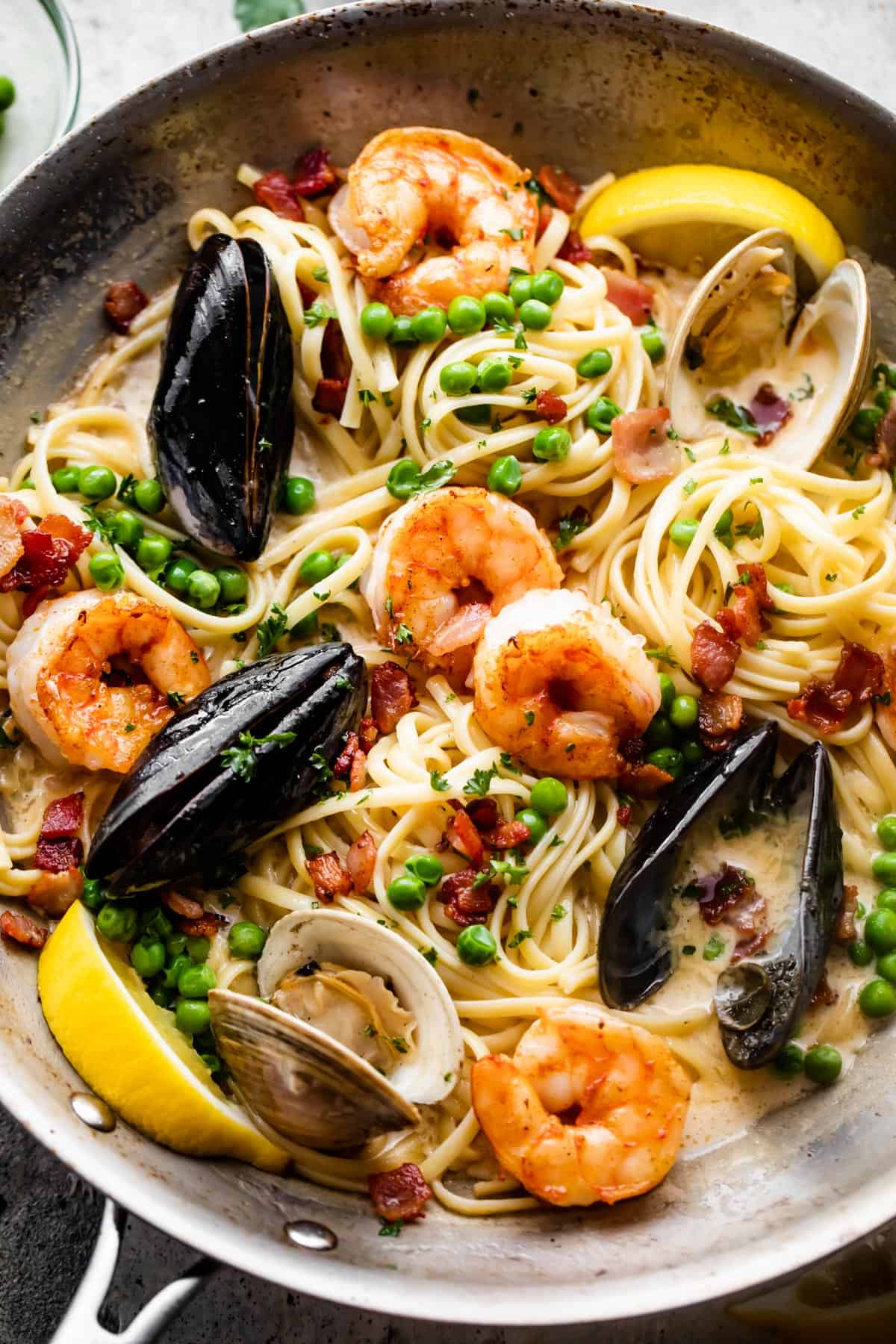 a skillet with pasta, shrimp, and mussels in cream sauce.