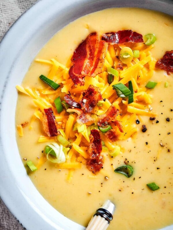 Close-up shot of bacon, green onions, and cheese sprinkled into a bowl of creamy soup.