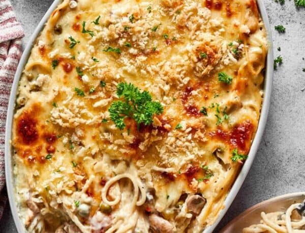 A large chicken tetrazzini casserole next to a dinner plate and a bunch of fresh herbs.