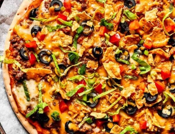 A baked taco pizza with toppings sprinkled over it.