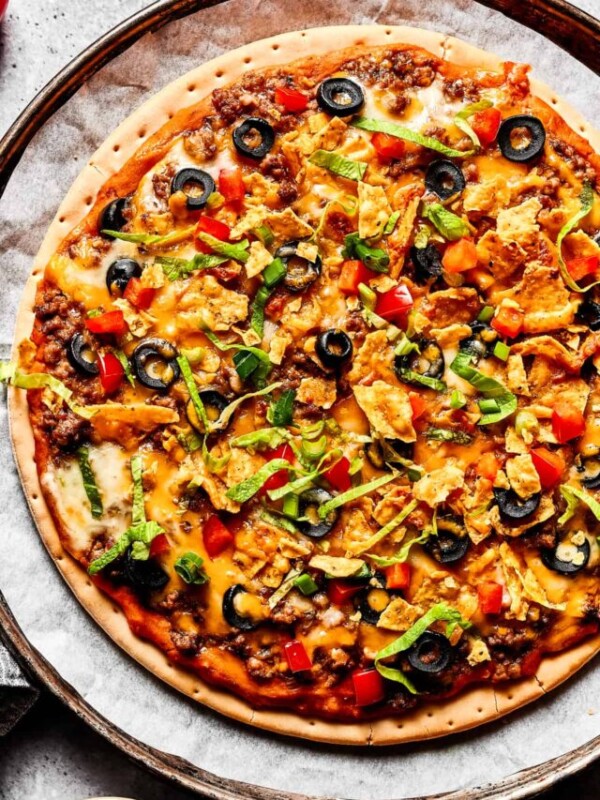 A baked taco pizza with toppings sprinkled over it.