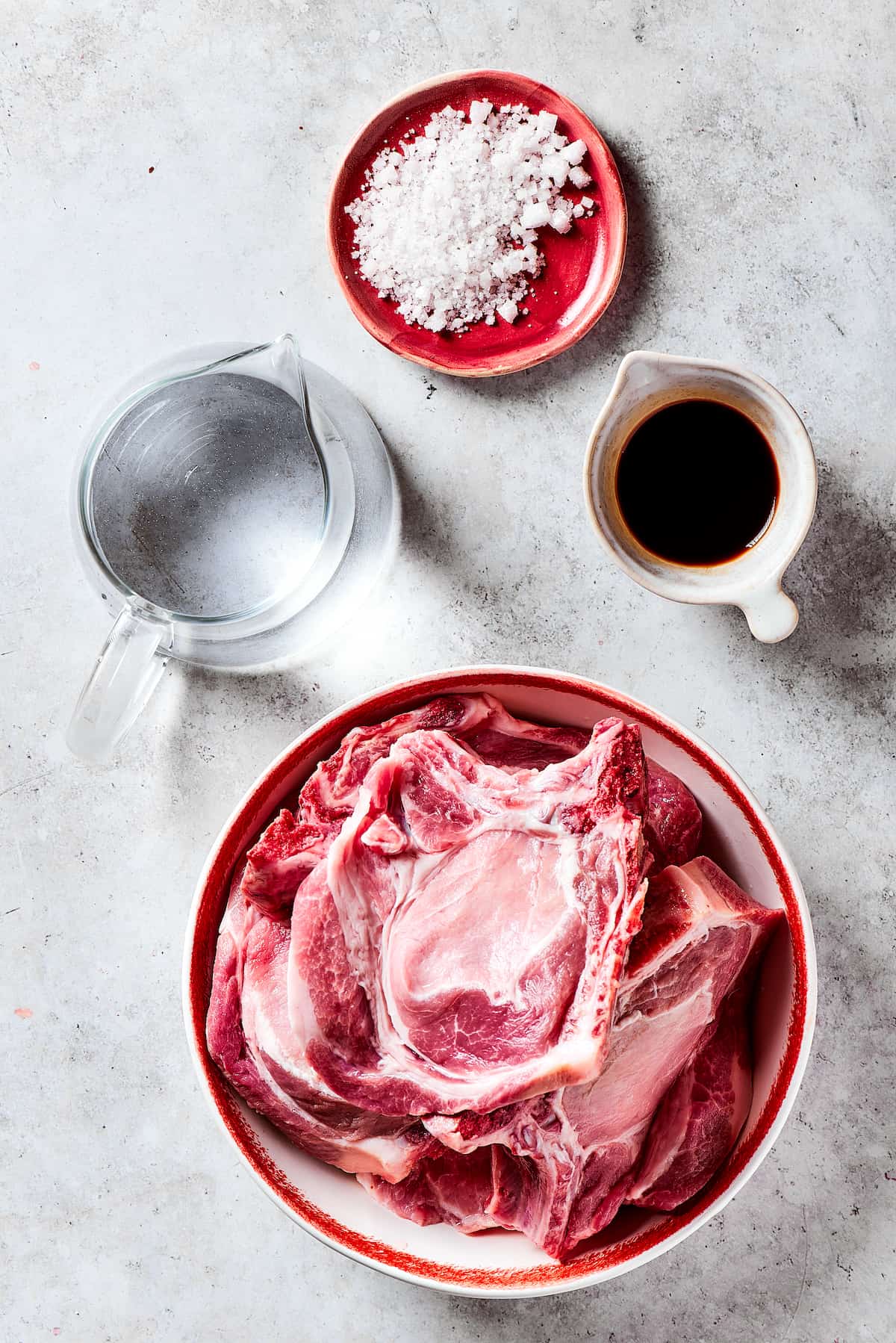 Preparing the Brine for Pork Chops Ingredients for brining: pork chops, salt, water, and balsamic vinegar laid out.