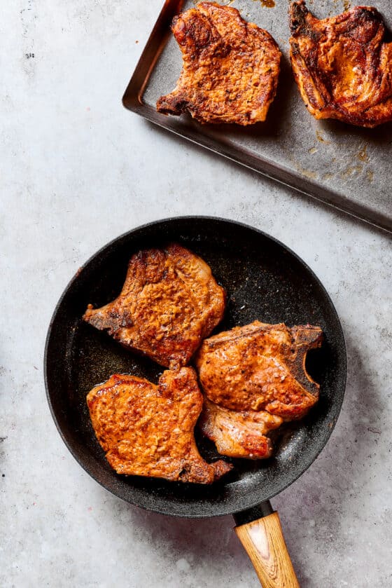 Browned pork chops in a skillet and other set aside on a tray.