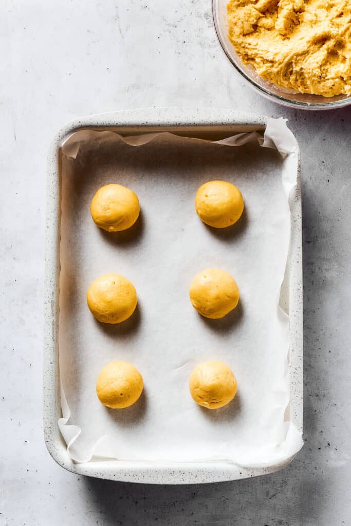 Balls of cookie dough on a parchment-lined baking sheet.