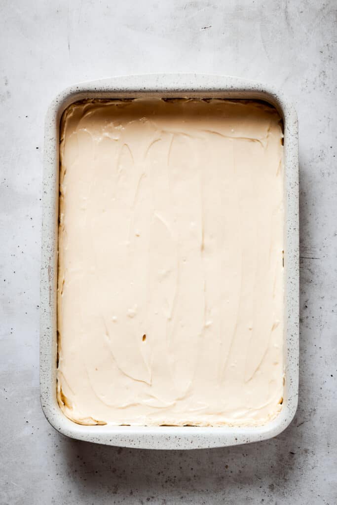 A baking dish with dough on the bottom and cream cheese filling spread in an even layer.