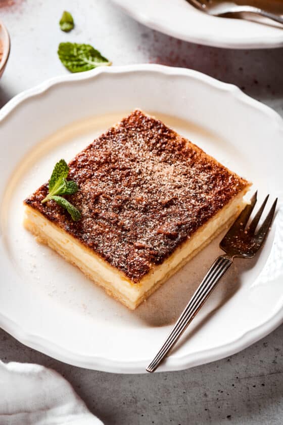 A square of cheesecake with cinnamon topping on a plate.