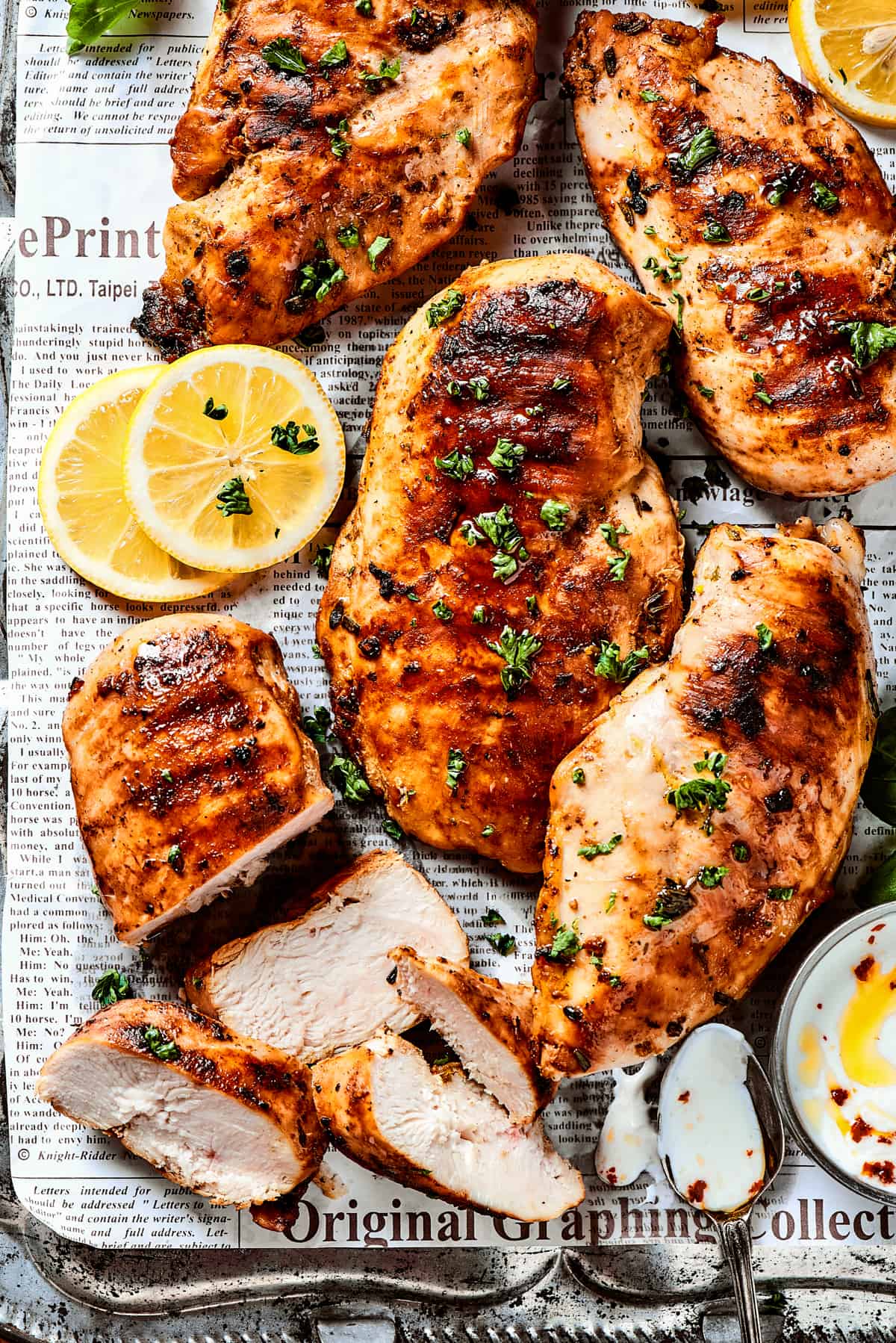 A sheet pan of lemon chicken with fresh herbs and lemon slices.